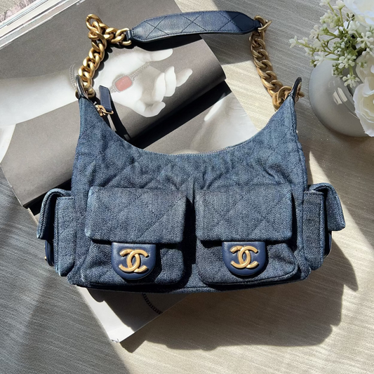 Blue handbag with gold chain strap on a wooden surface with flowers in the background