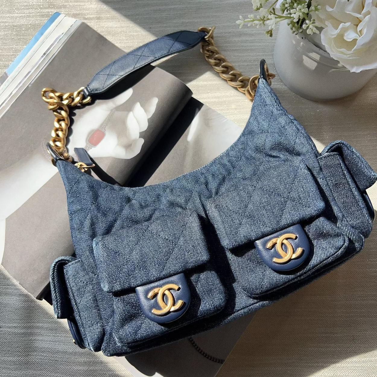 Blue quilted handbag with gold hardware on a wooden surface with flowers in the background