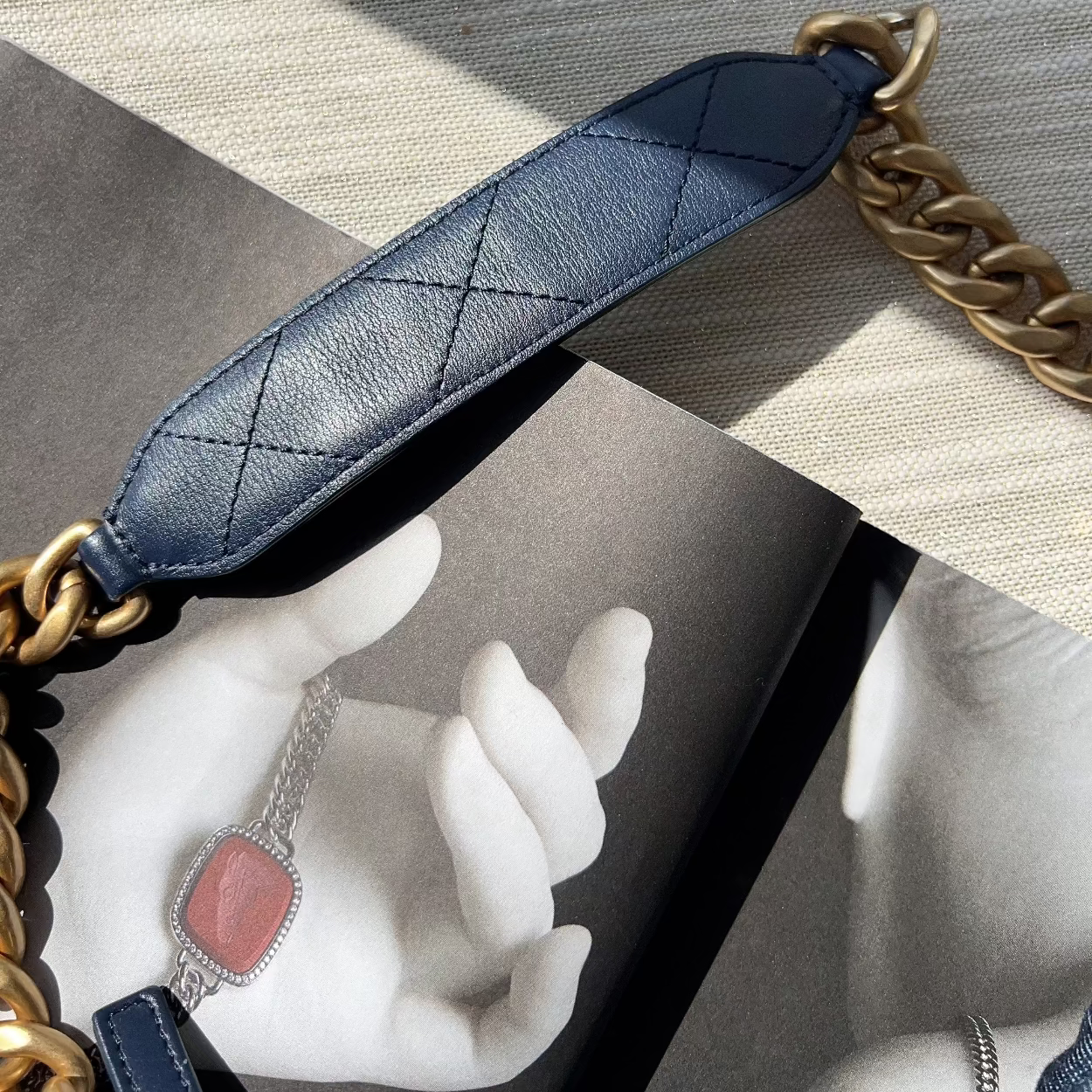 Close-up of a blue quilted leather strap with gold chain on a textured surface.