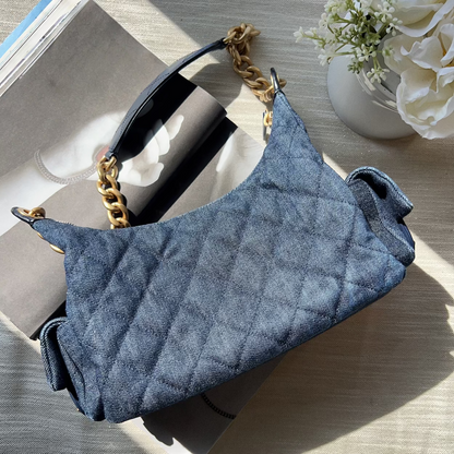 Blue handbag with gold chain handle on a wooden surface with flowers in the background
