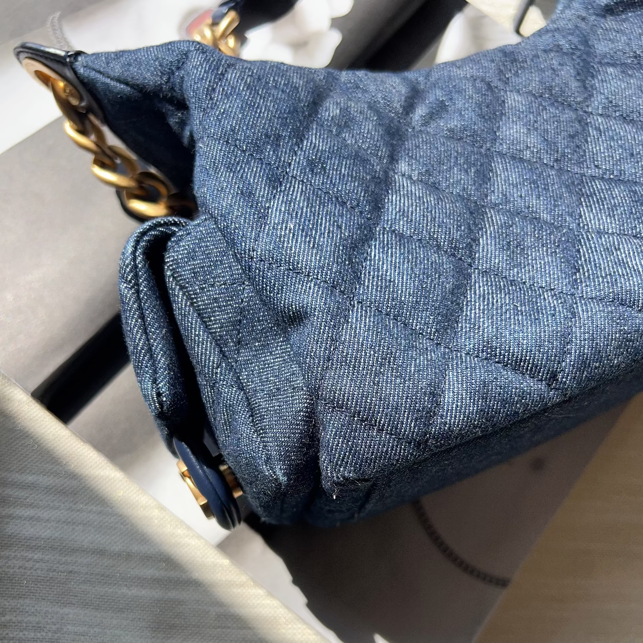 Close-up of a blue quilted handbag with gold accents on a light gray surface.
