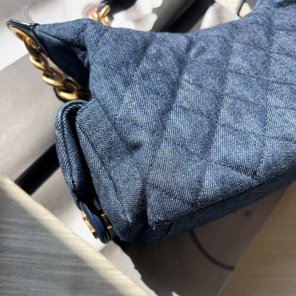 Close-up of a blue quilted handbag with gold accents on a light gray surface.