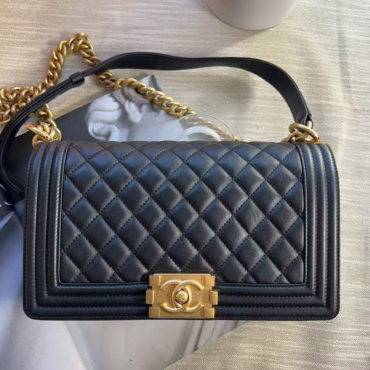 A black quilted leather shoulder bag with gold-tone hardware, featuring a top handle, chain strap, and a prominent interlocking CC clasp on the front, photographed on a light textured surface.