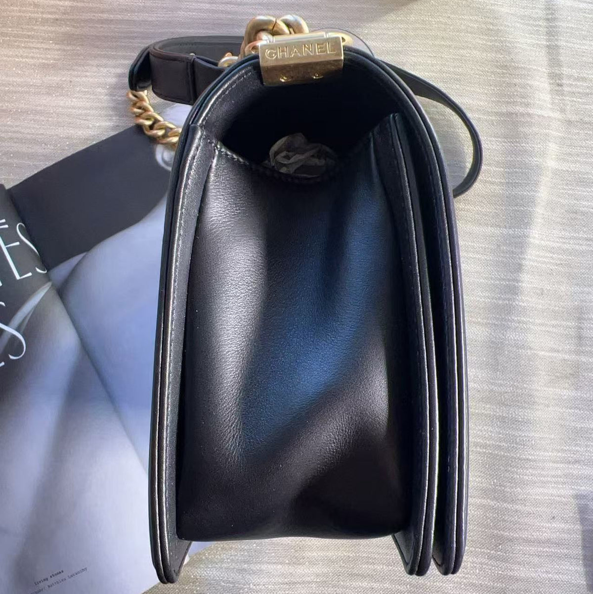 A black leather shoulder bag with a gold-tone chain strap and a gold padlock closure engraved with the brand name, shown from a top-down view on a light textured surface.