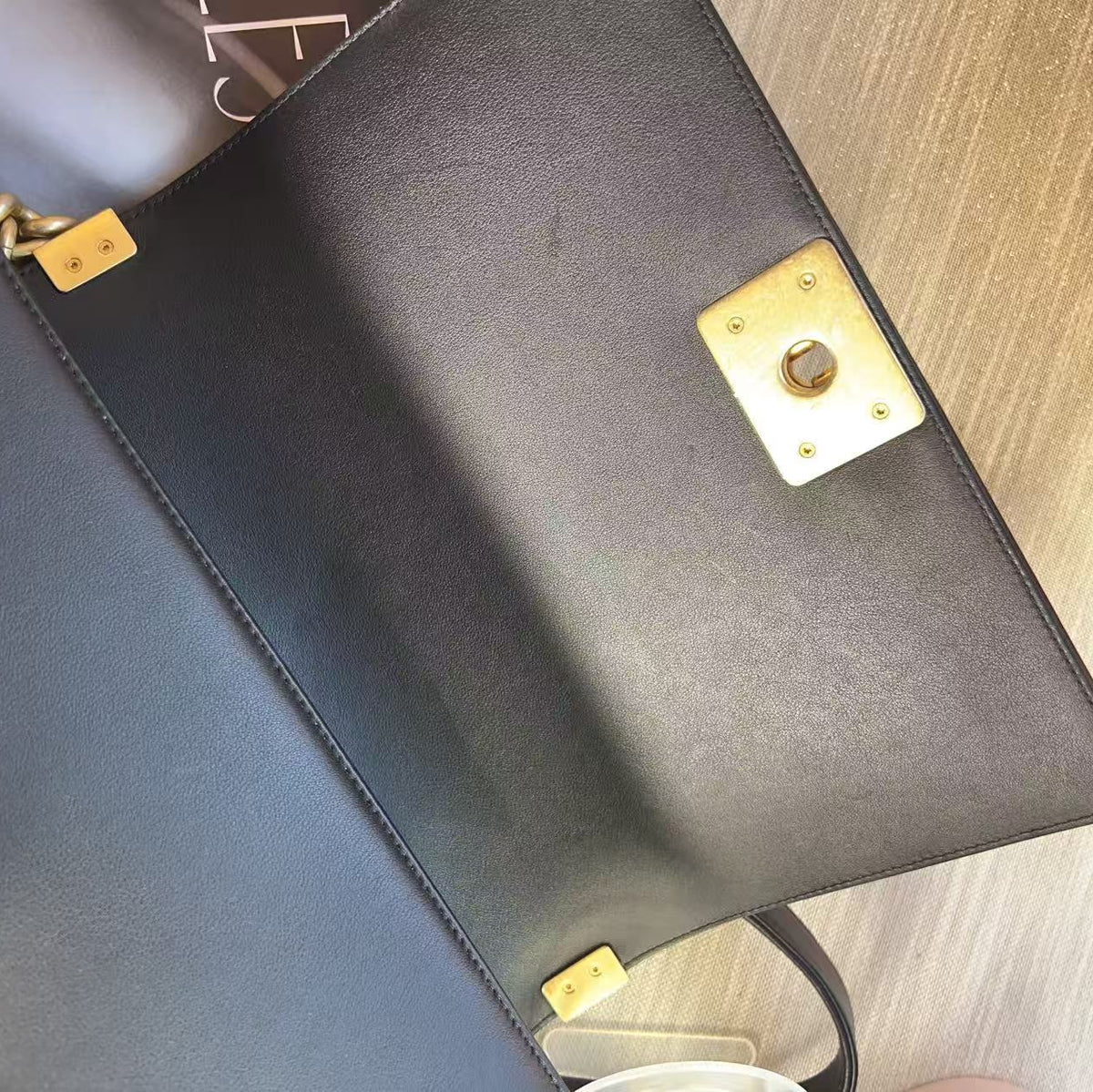 Close-up of a black leather handbag interior showing a gold-tone metal clasp and hardware on a light wood surface.