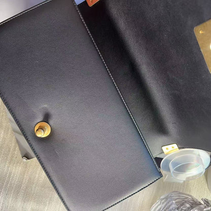 A close-up top-down view of a black leather clutch or wallet with gold-tone hardware, showing the interior flap, snap button, and a small clear plastic insert.