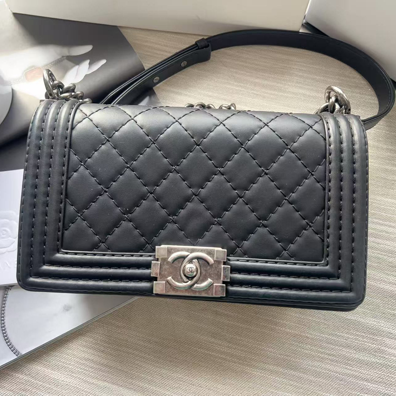 Black quilted handbag with silver clasp on a light gray surface