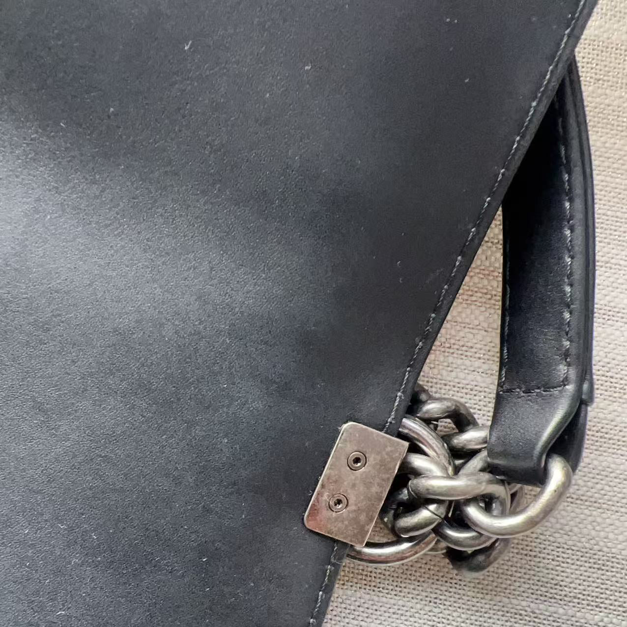 Close-up of a black leather bag with a chain detail on a beige surface