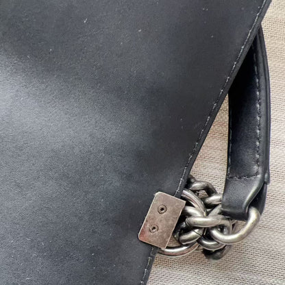 Close-up of a black leather bag with a chain detail on a beige surface