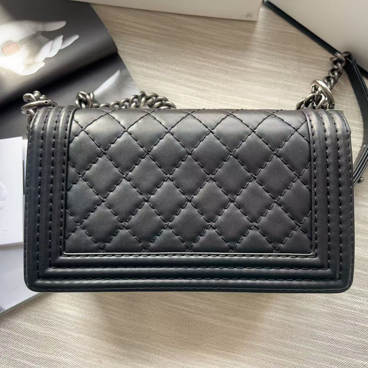 Black quilted handbag on a light wooden surface with a white card featuring a logo.