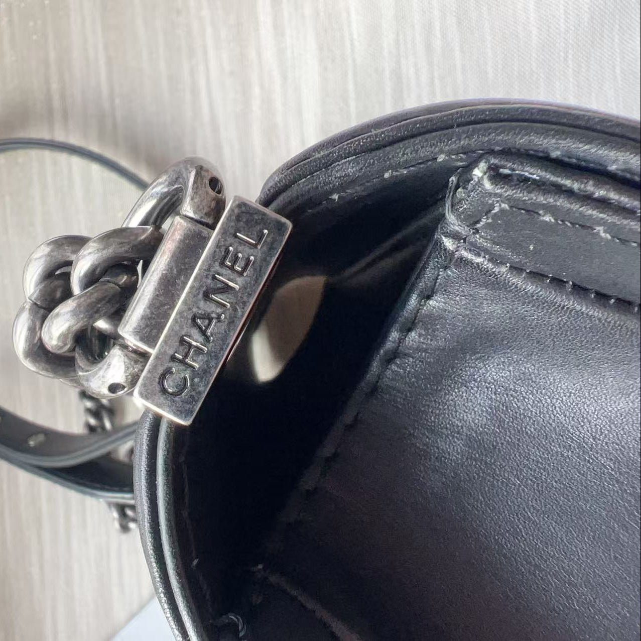 Close-up of a Chanel keychain attached to a black leather bag on a light wooden surface.