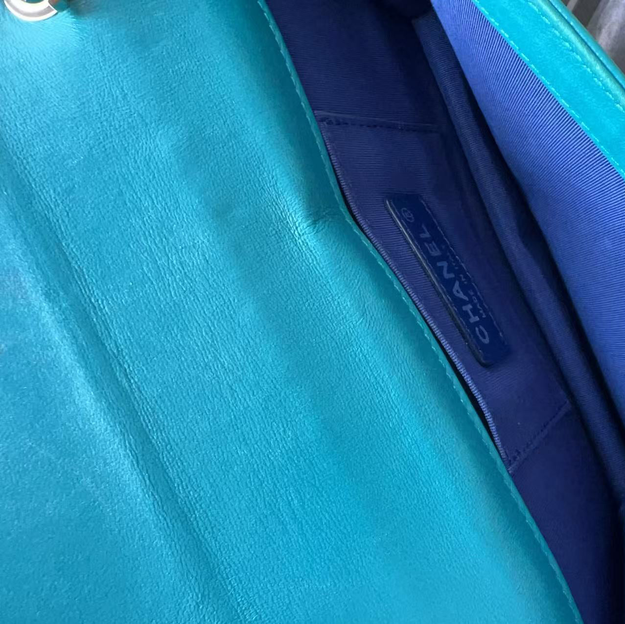 Close-up of a Chanel handbag interior showing a turquoise blue exterior, a dark blue interior lining, and a visible CHANEL label.