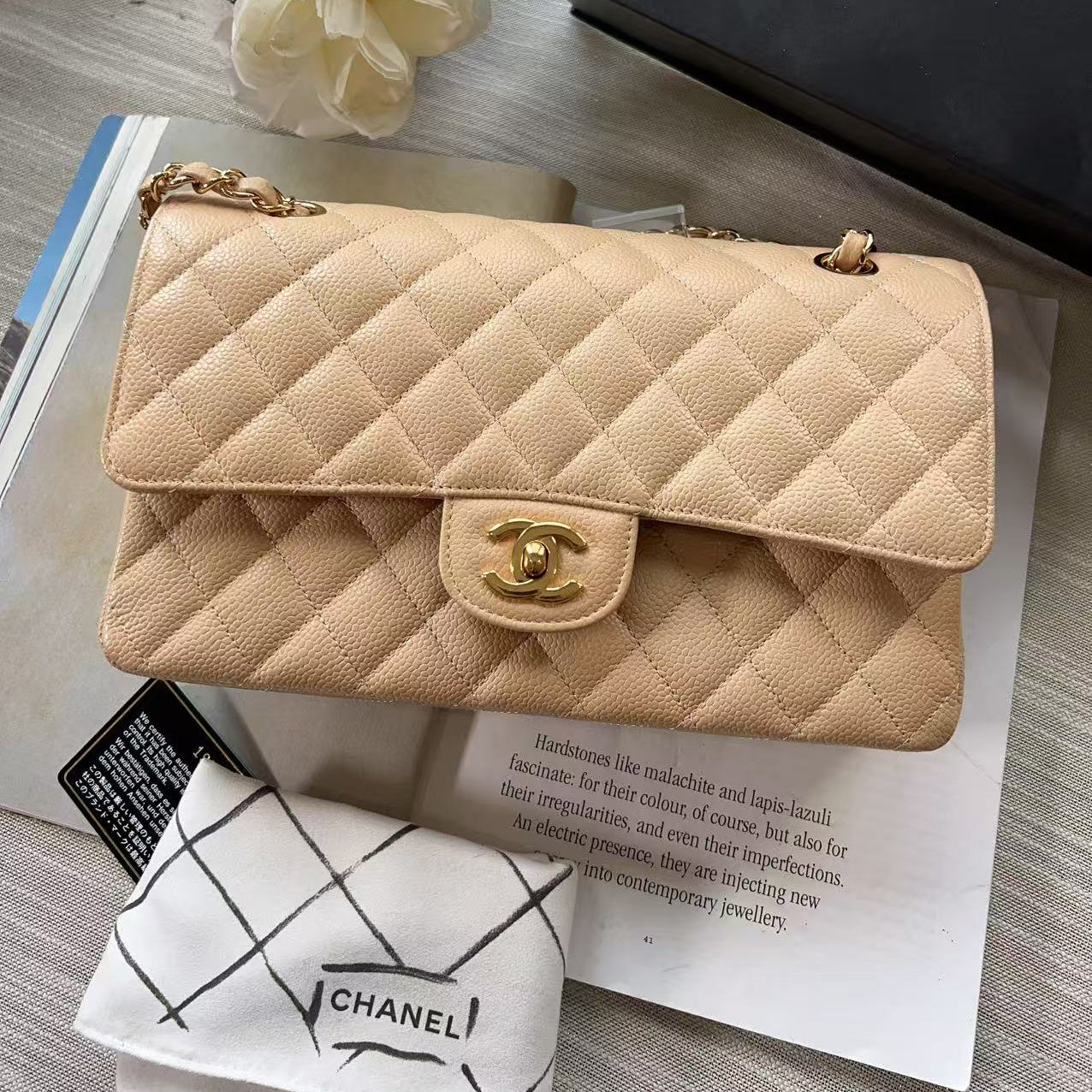 Beige quilted handbag with gold hardware on a magazine with a Chanel towel and box.