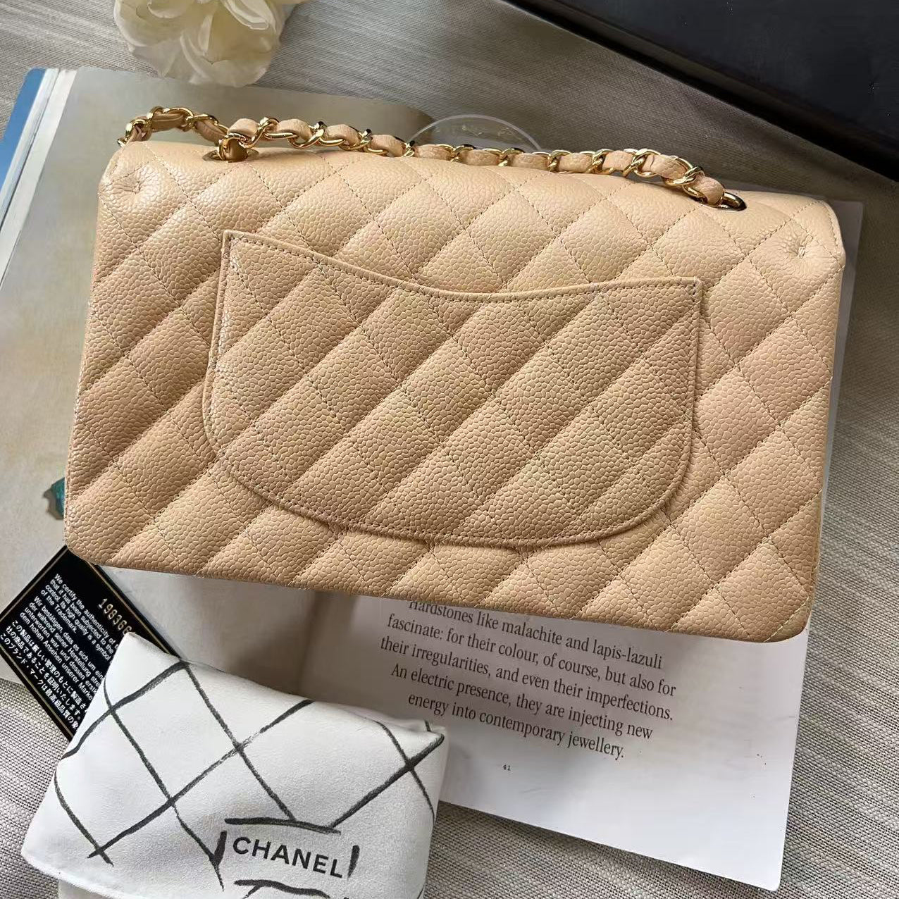 Beige quilted handbag with gold chain on a magazine with Chanel branding.