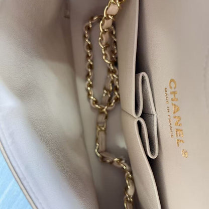 Close-up of a beige Chanel handbag with a gold chain strap on a light blue background.