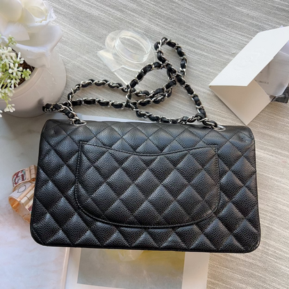 Black quilted handbag with a chain strap on a light wooden surface with flowers and an open book.