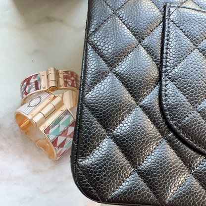 Black quilted handbag with colorful bracelets on a marble surface