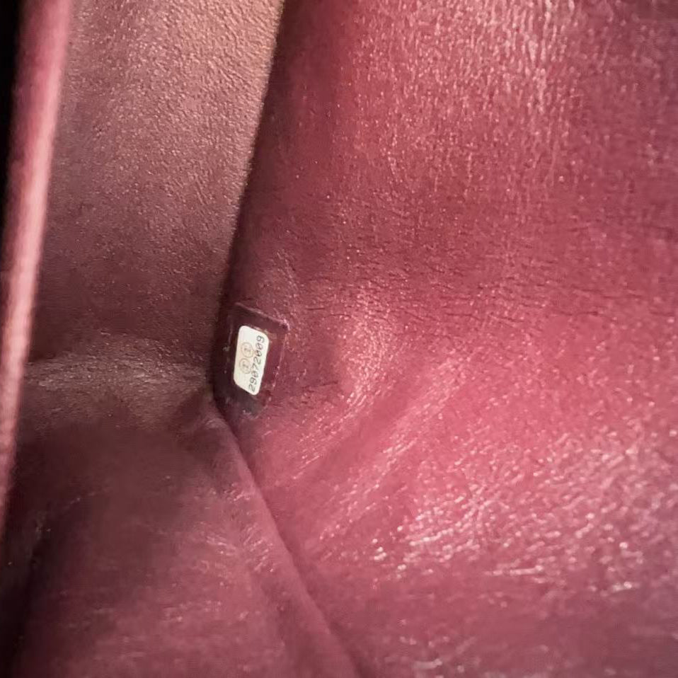A close-up shot of a burgundy leather interior pocket showing a small silver metal tag with a white label.