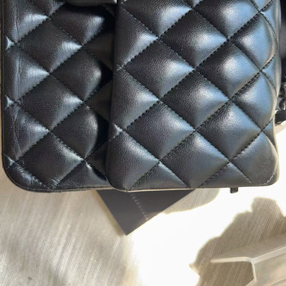 A close-up of a black quilted leather handbag with a diamond pattern, resting on a light-colored fabric surface.