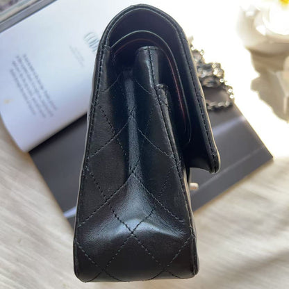A close-up of a black quilted leather handbag, showing the texture and stitching, resting on a dark book or box with an open magazine in the background.