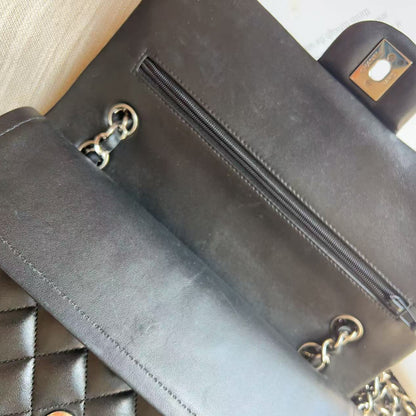 Close-up of a dark brown leather wallet or clutch showing the interior zip pocket, chain hardware, and quilted exterior pattern.