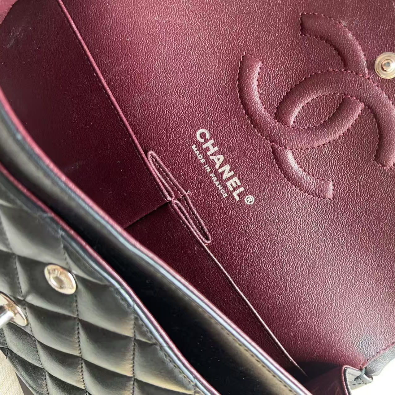 Close-up of a Chanel handbag interior showing a burgundy leather lining with an embossed interlocking CC logo and CHANEL MADE IN FRANCE text, alongside a black quilted exterior.