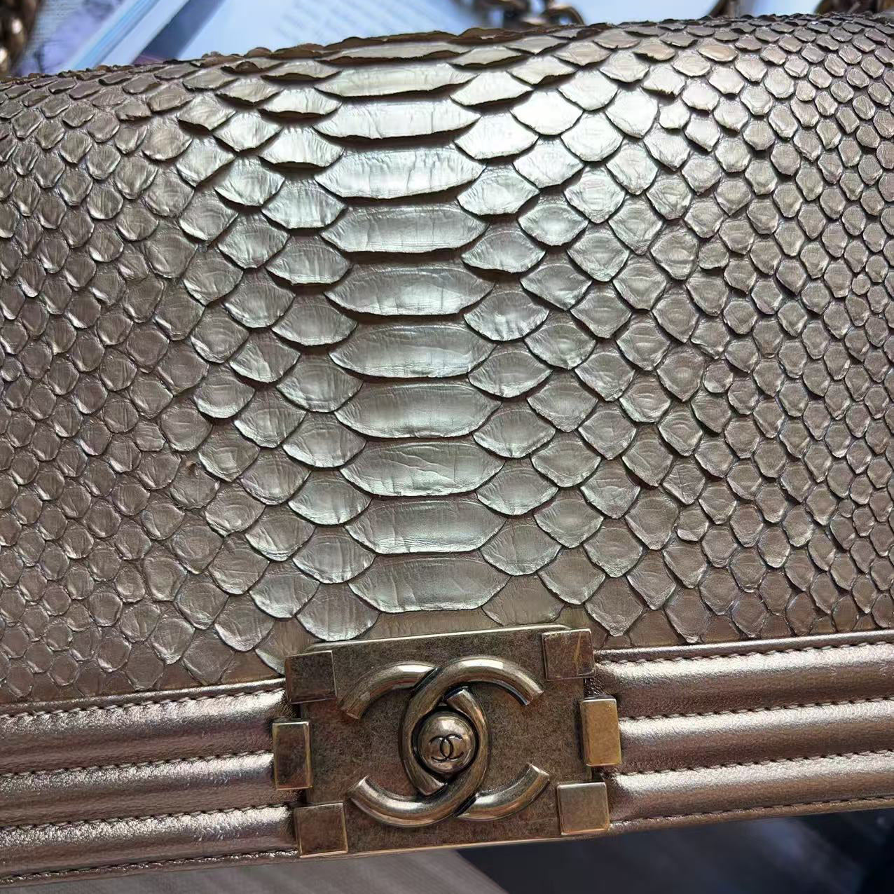 Close-up of a metallic gold snakeskin handbag with a gold-tone interlocking CC clasp, showing the scale pattern and hardware detail.