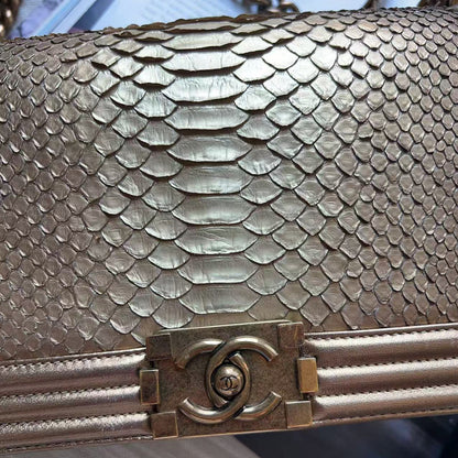 Close-up of a metallic gold snakeskin handbag with a gold-tone interlocking CC clasp, showing the scale pattern and hardware detail.