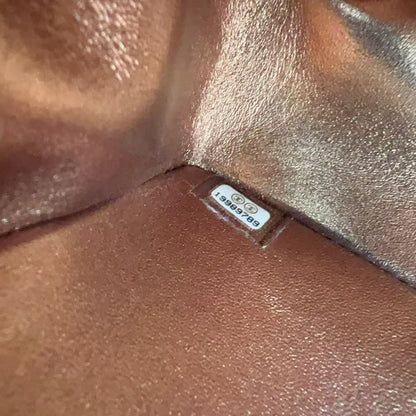 A close-up of a person's shoulder with a shimmering bronze metallic body paint or tattoo design, featuring a small white rectangular brand sticker that reads 'DEADLINE'.