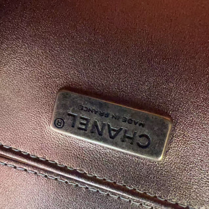 A close-up of a dark brown textured leather item featuring a rectangular metal plaque engraved with 'CHANEL MADE IN FRANCE'.