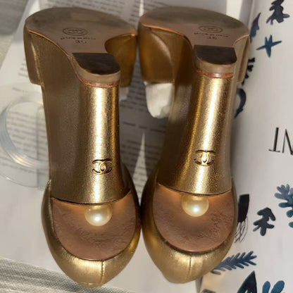 A pair of Chanel high-heeled shoes in metallic gold with a pearl detail on the toe, displayed on a magazine page.