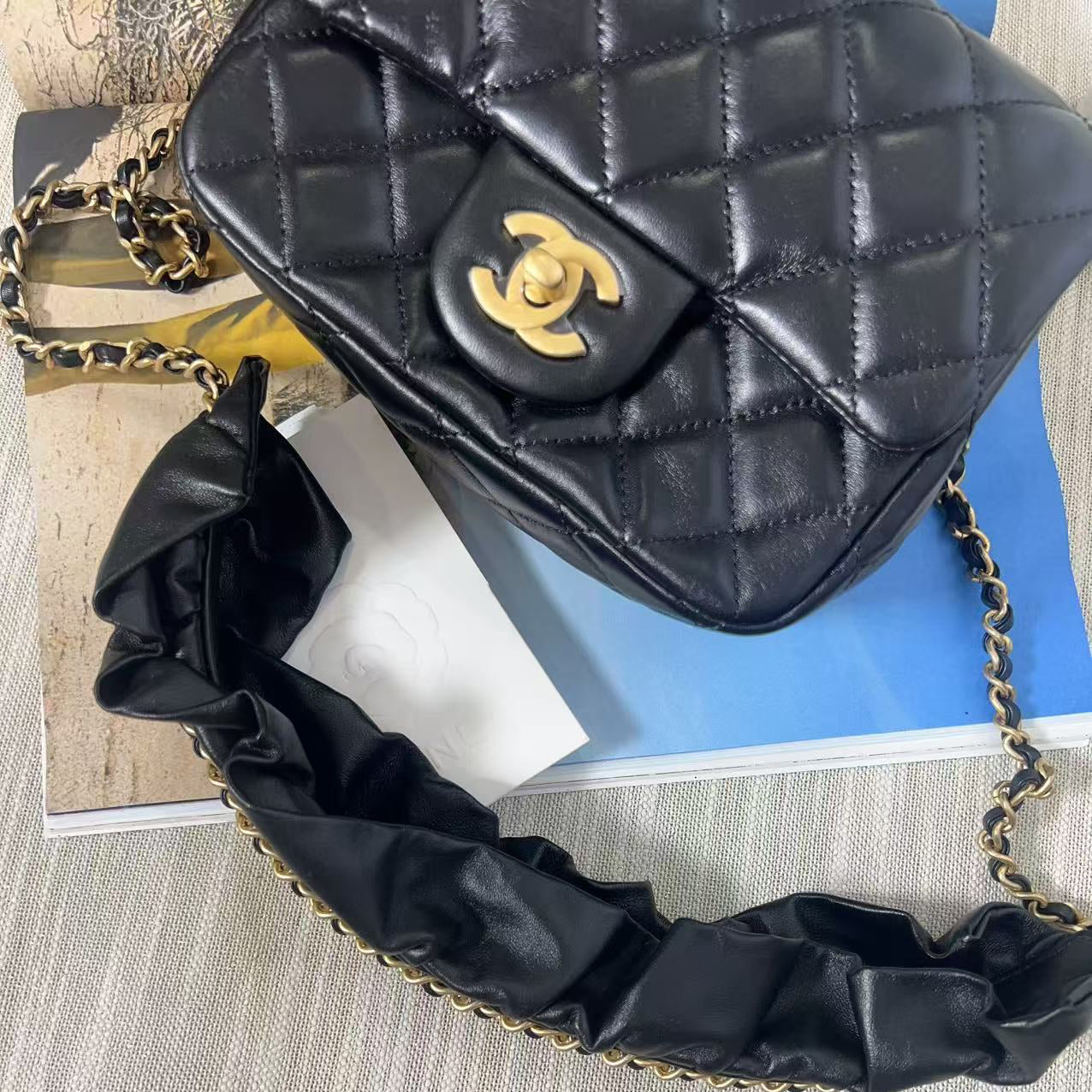 Black quilted handbag with gold chain strap on a textured surface
