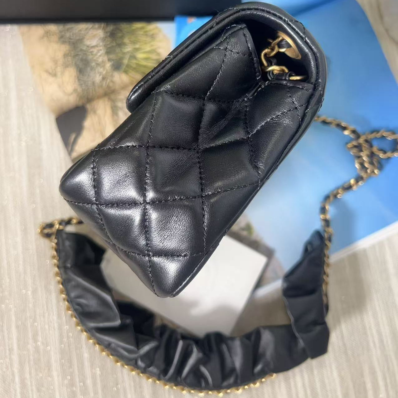 Black quilted handbag with gold chain on a textured surface