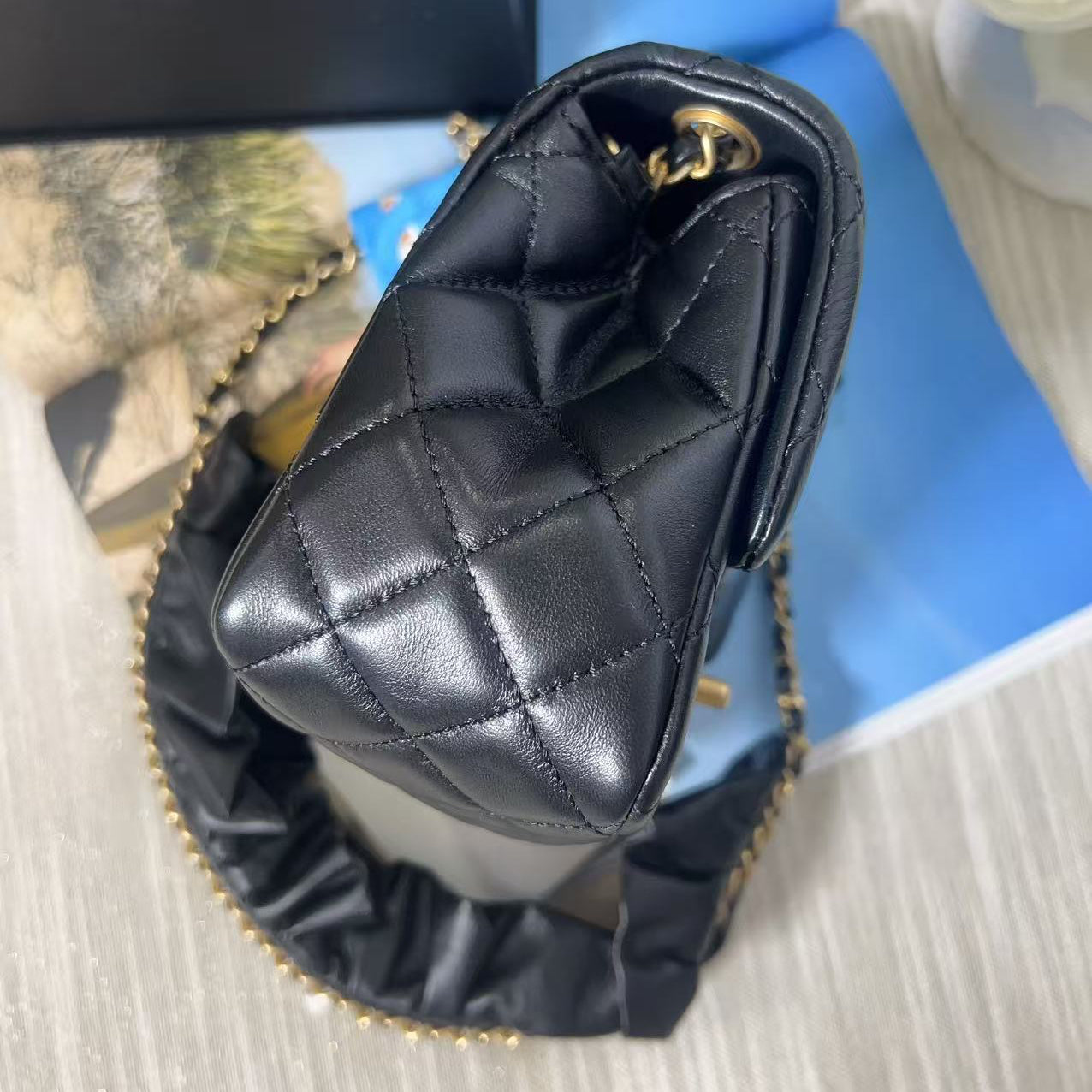 Black quilted handbag with gold chain on a textured surface