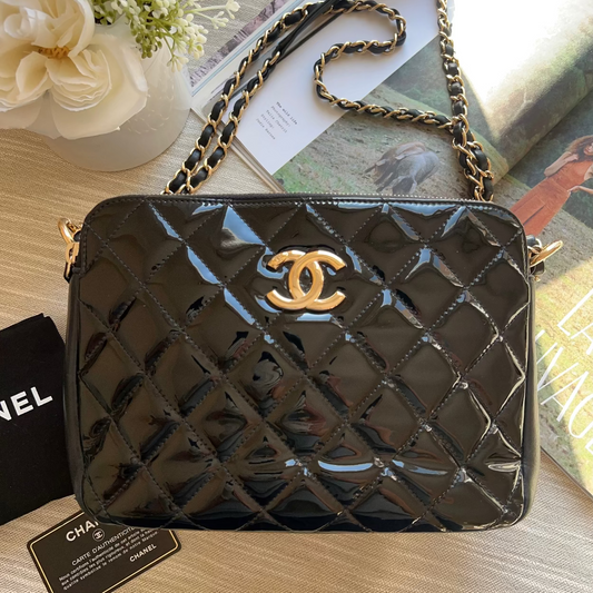 Black quilted handbag with gold chain strap on a wooden surface, featuring a Chanel tag.