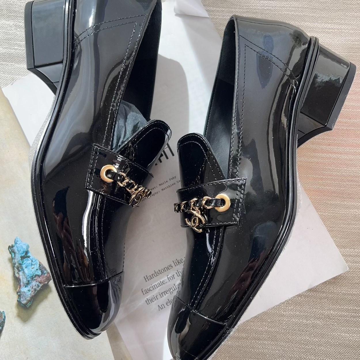 Black patent leather shoes with gold accents on a textured surface