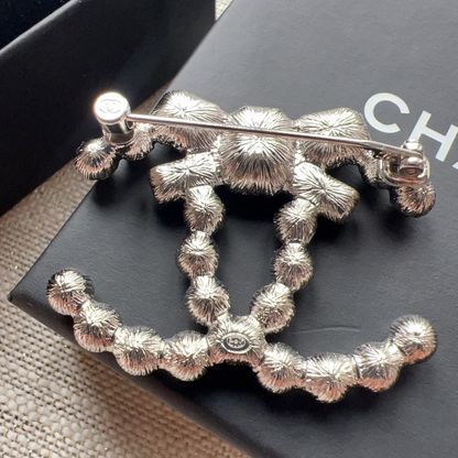 Silver brooch on a black surface with 'CHANEL' branding