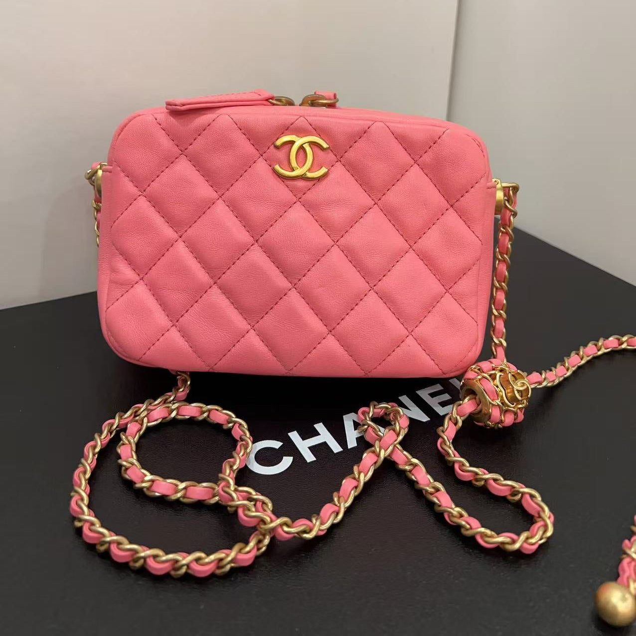 Pink quilted handbag with gold chain on a black surface