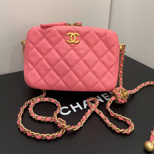 Pink quilted handbag with gold chain on a black surface
