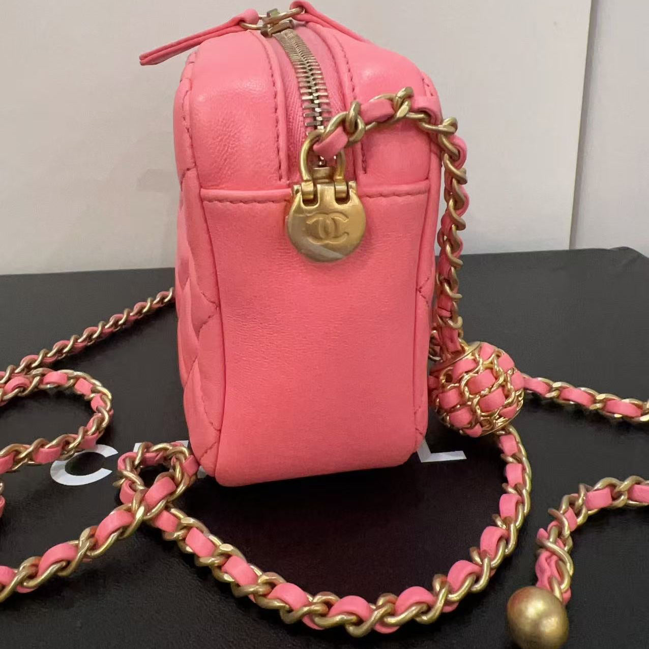 Pink handbag with gold chain strap on a black surface