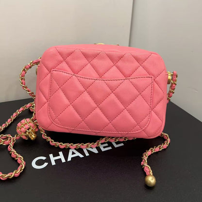 Pink quilted handbag with gold chain on a black surface with 'Chanel' branding.