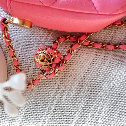 Pink handbag with gold chain strap on a textured surface with white flowers.