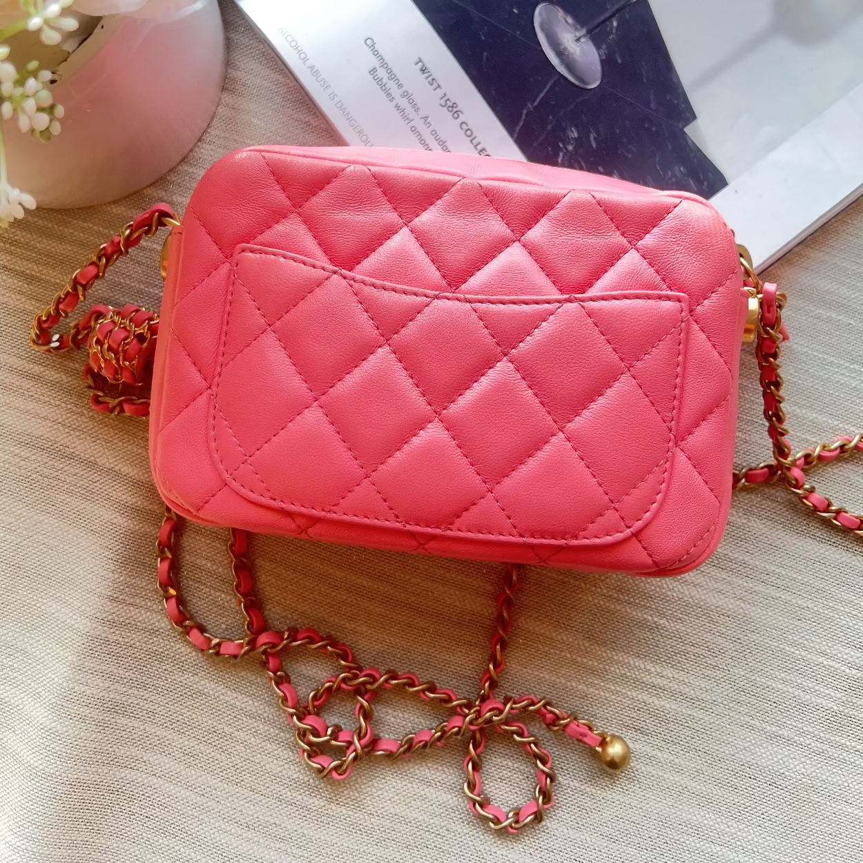 Pink quilted handbag with a chain strap on a textured surface