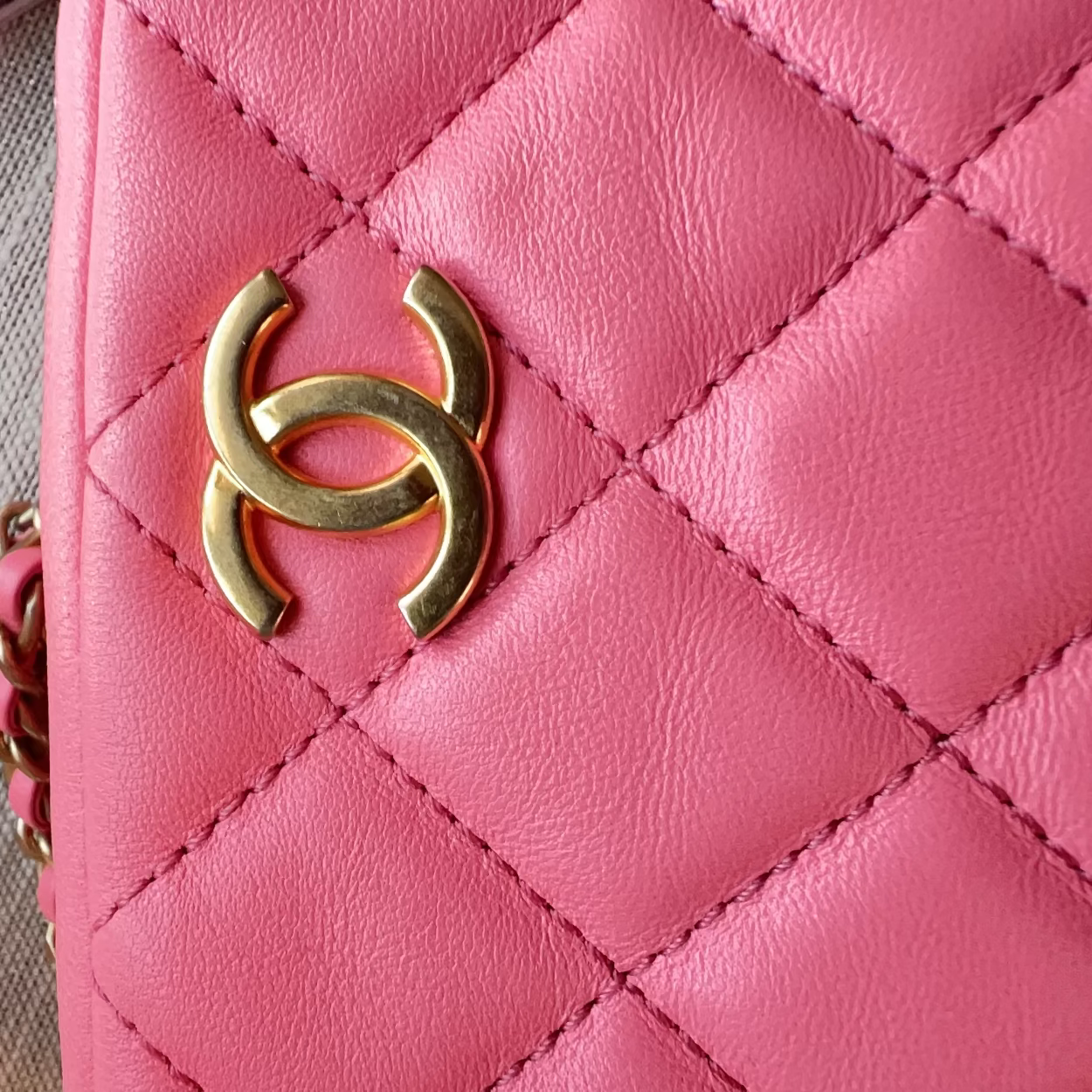Pink quilted handbag with gold logo on a textured surface