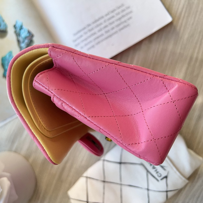 Pink and beige quilted leather wallets on a wooden surface with a book and decorative stones.
