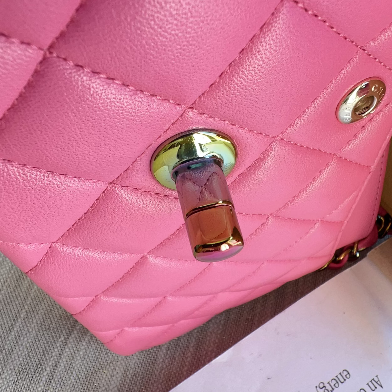 Close-up of a pink quilted handbag with a gold lock on a neutral background