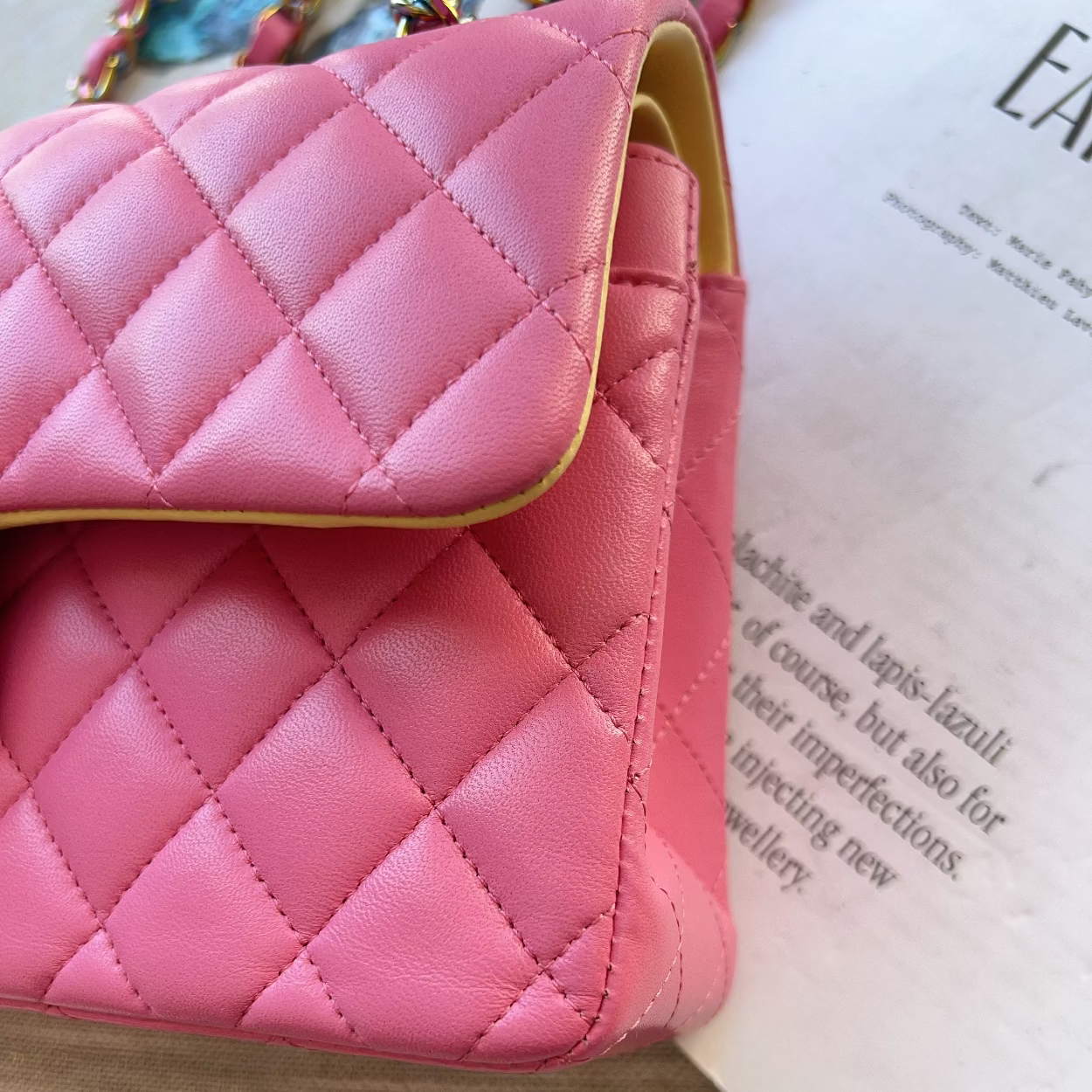 Pink quilted handbag on a textured surface with text partially visible