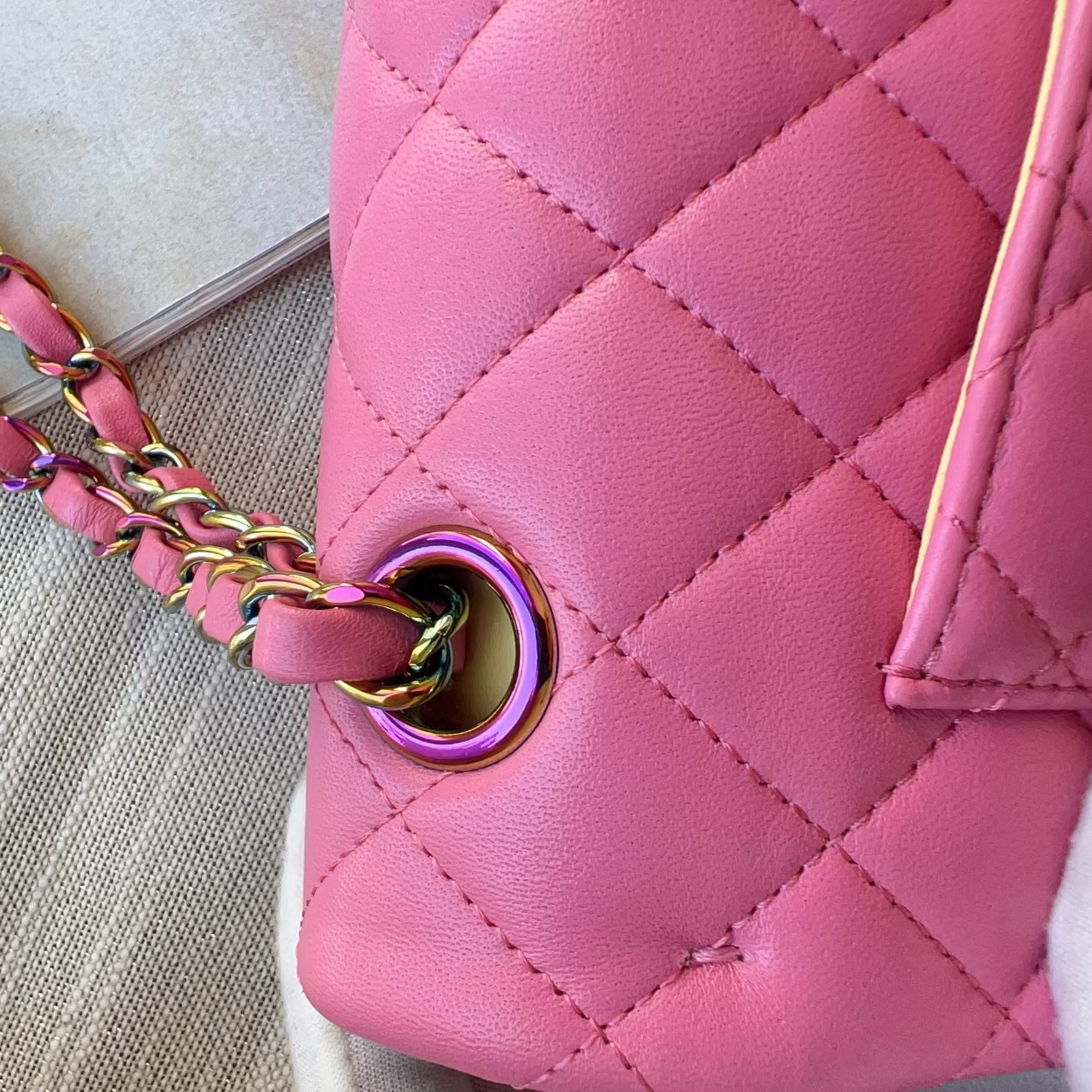 Close-up of a pink quilted handbag with a gold chain strap on a textured surface.