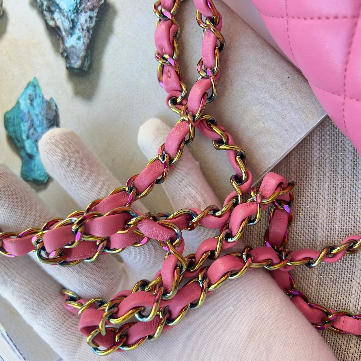 Close-up of pink chain belt with gold accents held by a hand, with a pink bag and stones in the background.