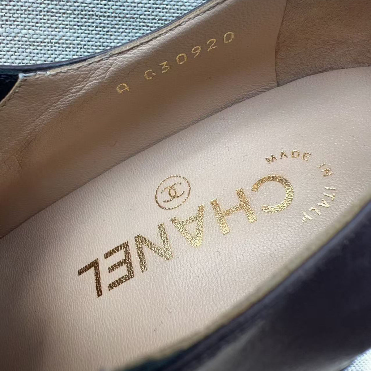 Close-up of the interior insole of a Chanel shoe, showing the gold CHANEL logo, 'MADE IN ITALY' text, and serial number 'A G30920' on a beige leather footbed, with a dark blue fabric exterior visible at the top.